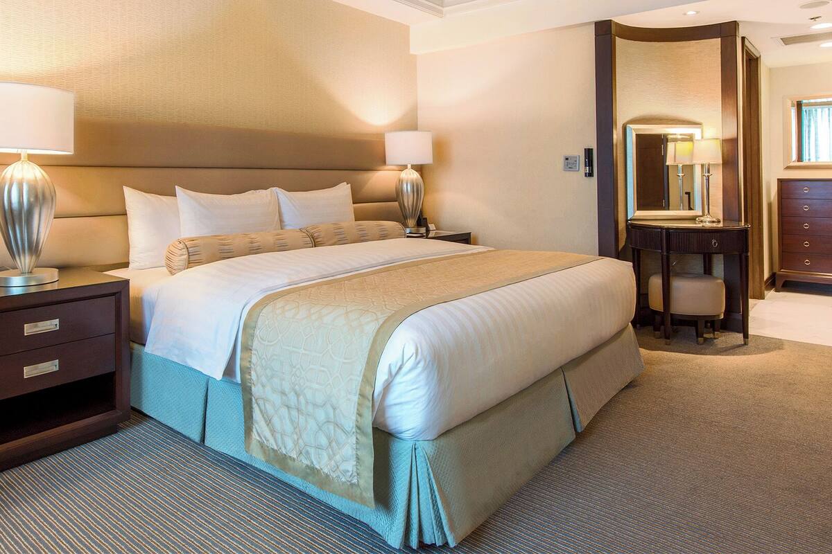 A hotel room with a large bed, two bedside tables with lamps, a dresser, and a mirror.
