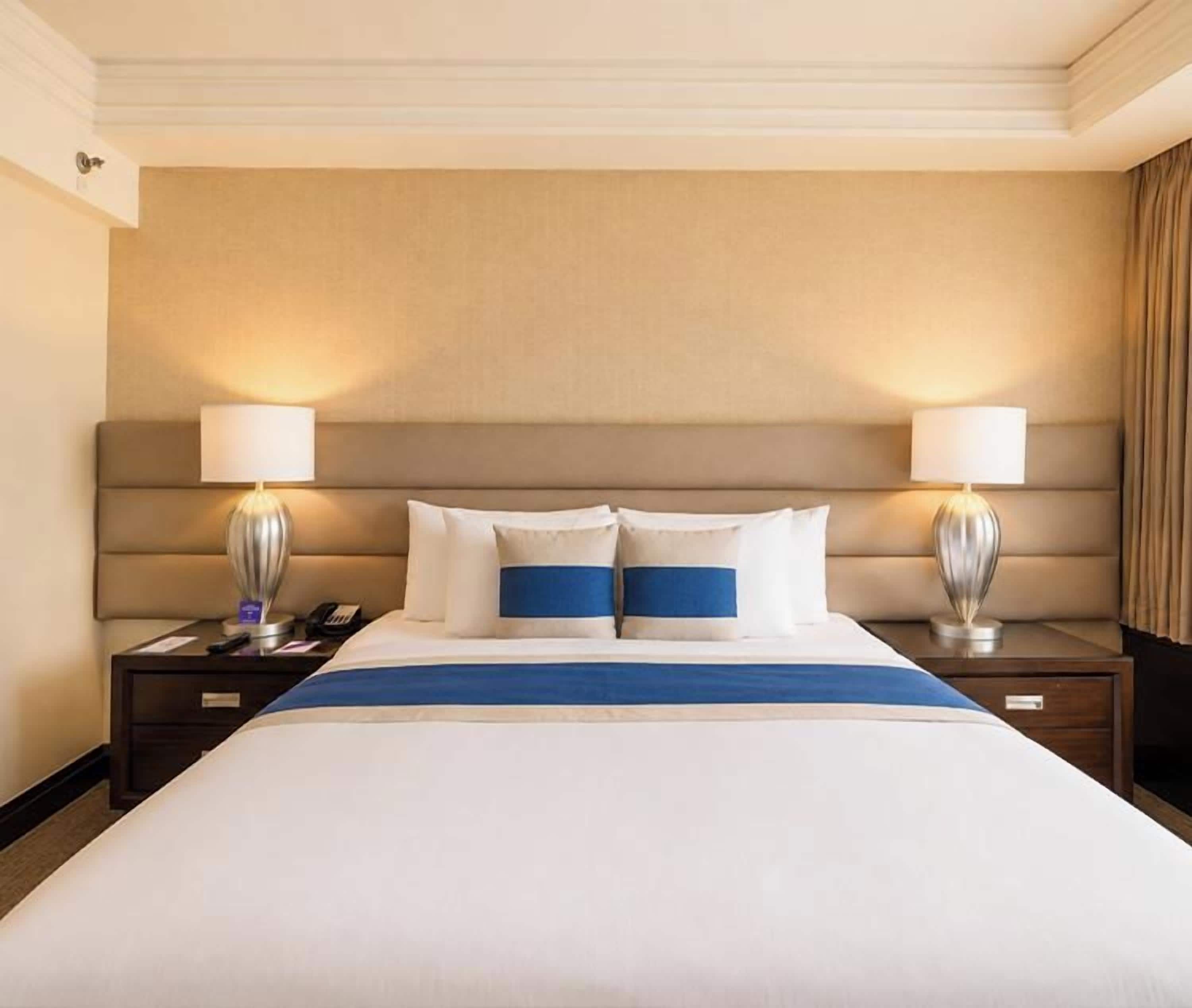 A hotel room with a large bed, two bedside lamps, and a headboard.
