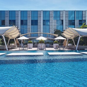 A modern hotel pool area with a clear view of the building facade, outdoor seating, and a central water feature. - Quest Plus Filinvest City Manila (Muntinlupa)