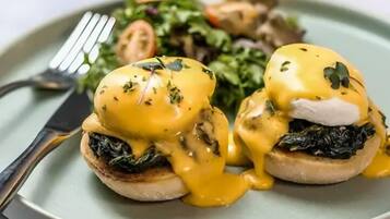 Un plato de huevos benedictinos con salsa holandesa, acompañado de una ensalada.