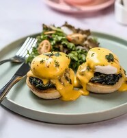 Un plato de huevos benedictinos con salsa holandesa, acompañado de una ensalada.