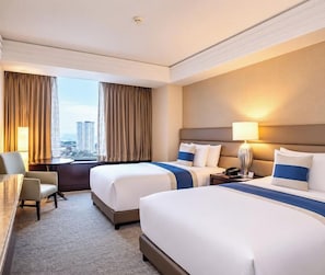 A hotel room with two beds, a desk, a chair, and a view of the city. - Quest Plus Filinvest City Manila (Muntinlupa)