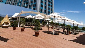 A modern building with a reflective glass facade, outdoor seating area with umbrellas, and potted plants.