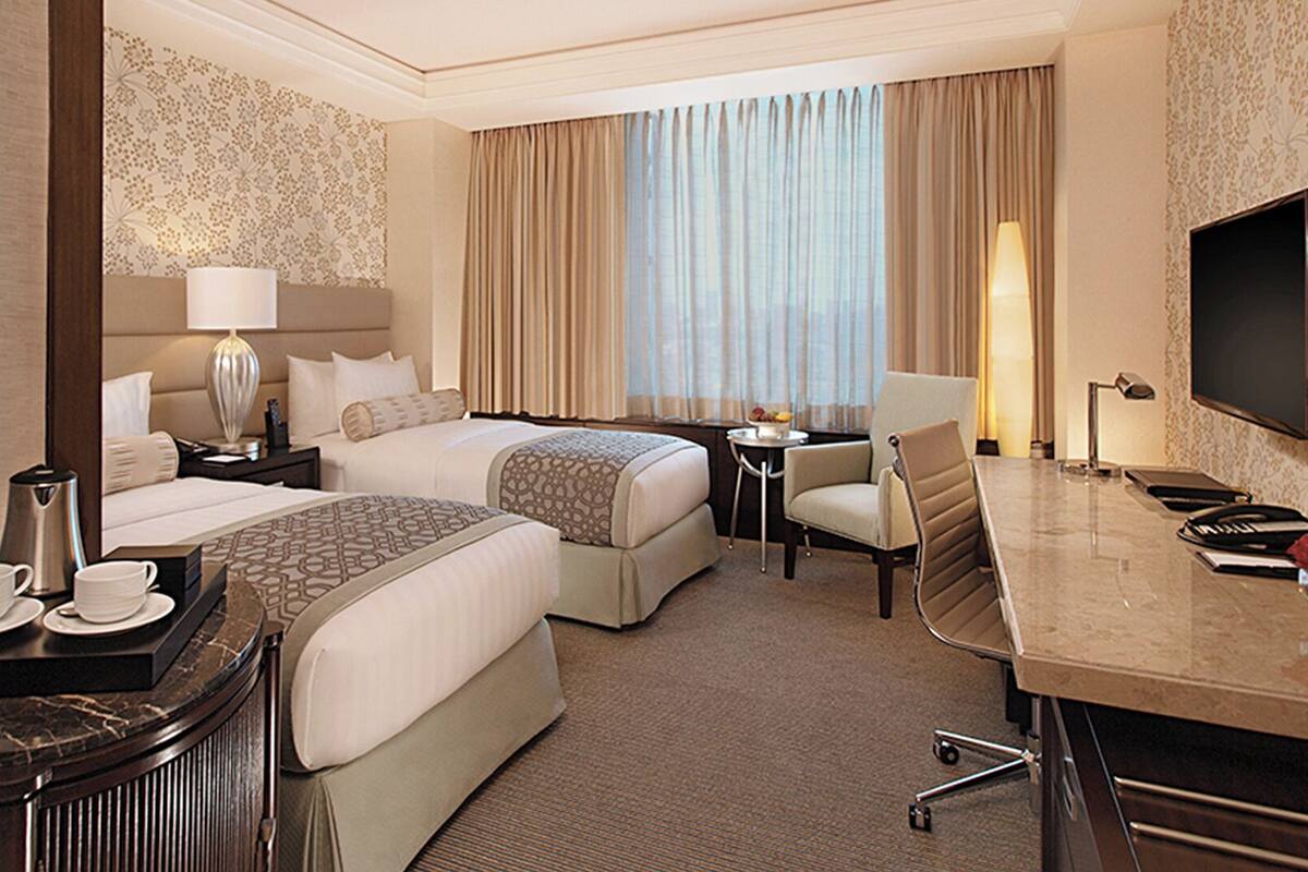 A hotel room with two beds, a desk, a chair, a TV, and a coffee maker.