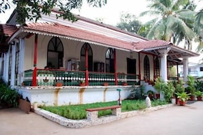 Um edifício em estilo colonial com varanda, colunas e telhado com telhas.