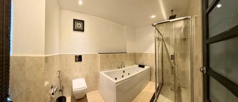 A modern bathroom with a bathtub, toilet, and glass-enclosed shower.