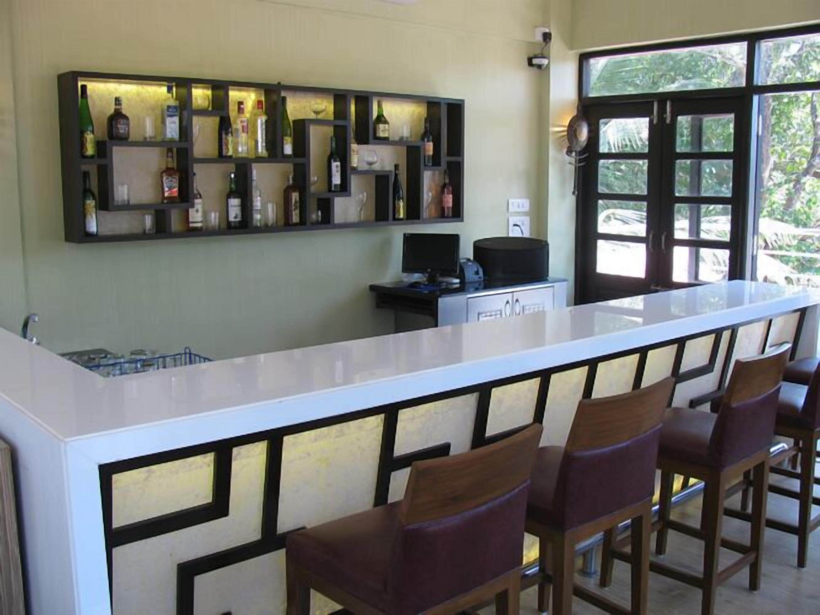 Un espace bar doté d’un comptoir blanc, de nombreuses bouteilles d’alcool et de tabourets de bar.