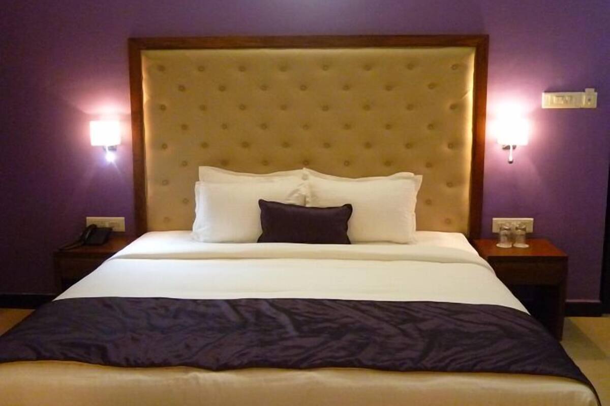 Una habitación de hotel con una cama grande, un cabecero acolchado y dos lámparas de noche.