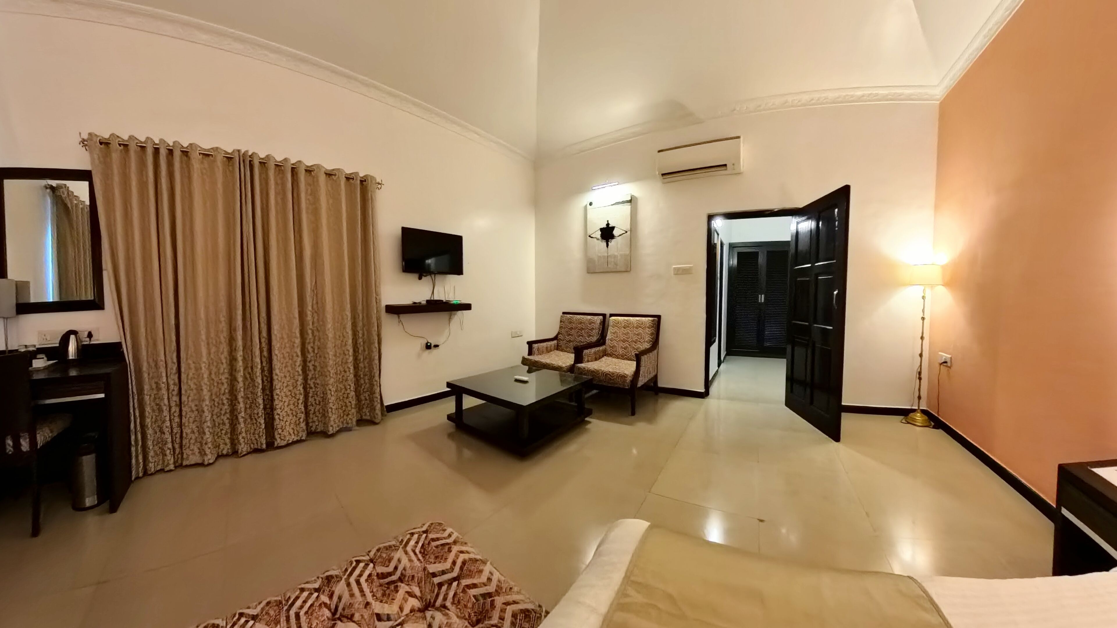 A hotel room with a flat-screen TV, a sofa, a coffee table, and a bed.