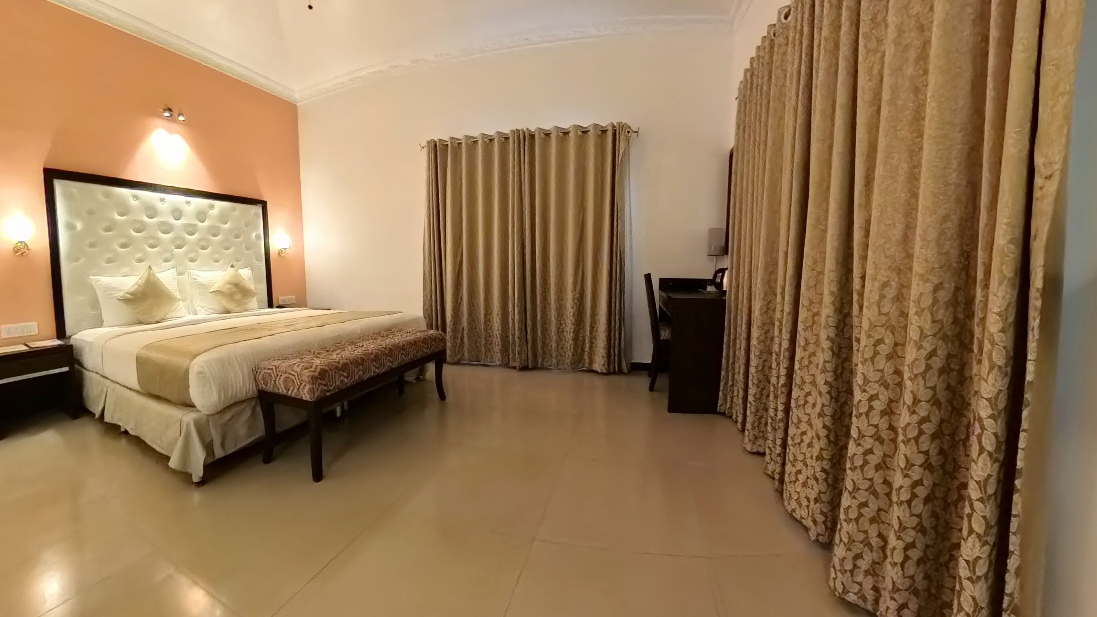 A hotel room with a large bed, a bench, a desk, and curtains.
