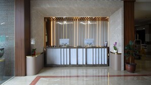 Un comptoir d’accueil moderne, doté d’un plateau en marbre, de lambris en bois verticaux et de deux plantes en pot.