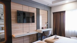 Une chambre d’hôtel avec deux lits, un bureau, une chaise, une télévision et une grande fenêtre avec des rideaux.