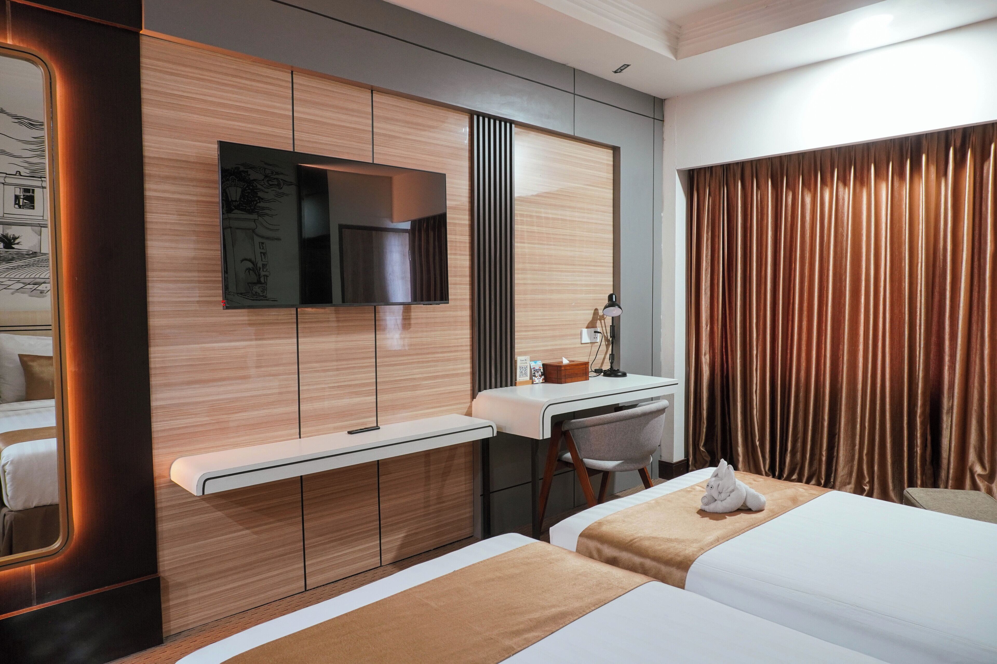 A hotel room with a bed, a desk, a chair, a TV, and a window with curtains.