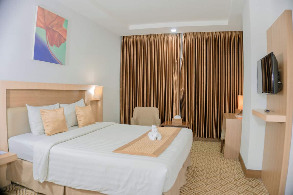 Habitación de hotel con una cama, una silla, un escritorio, un televisor y una cortina.