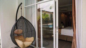 Un fauteuil suspendu avec des coussins, une porte-fenêtre coulissante donnant sur une chambre, et une piscine visible.