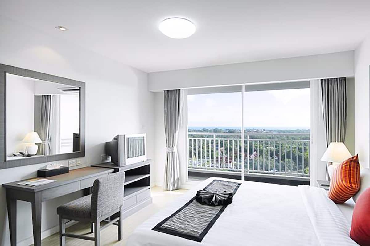 Ein Hotelzimmer mit einem großen Bett, einem Schreibtisch, einem Sessel, einem Fernseher und einem Balkon mit Aussicht.