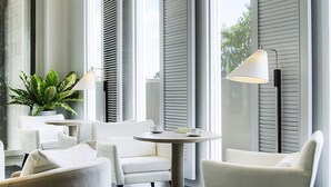 A modern, well-lit room with white furniture, large windows with blinds, and a potted plant. - Classic Kameo Hotel & Serviced Apartments, Rayong (Rayong)