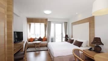 A hotel room with a large bed, a desk, a television, and a sofa with a view of the city.