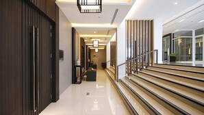 A modern hotel corridor with a wooden door, a staircase, and a view of the outside through large windows. - Classic Kameo Hotel & Serviced Apartments, Rayong (Rayong)