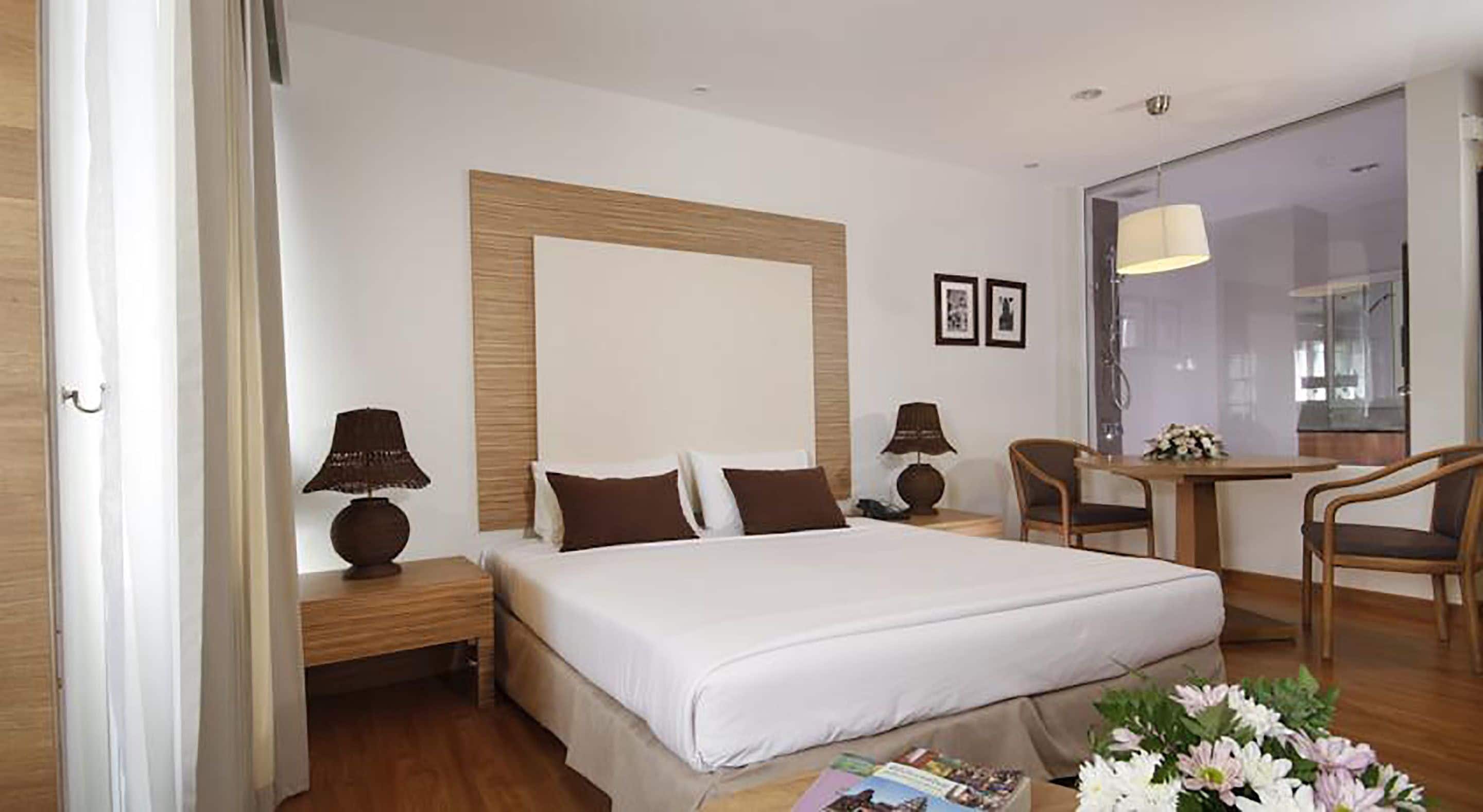 Habitación de hotel con una cama grande, dos mesitas de noche, un escritorio con una silla y una ventana con vistas.