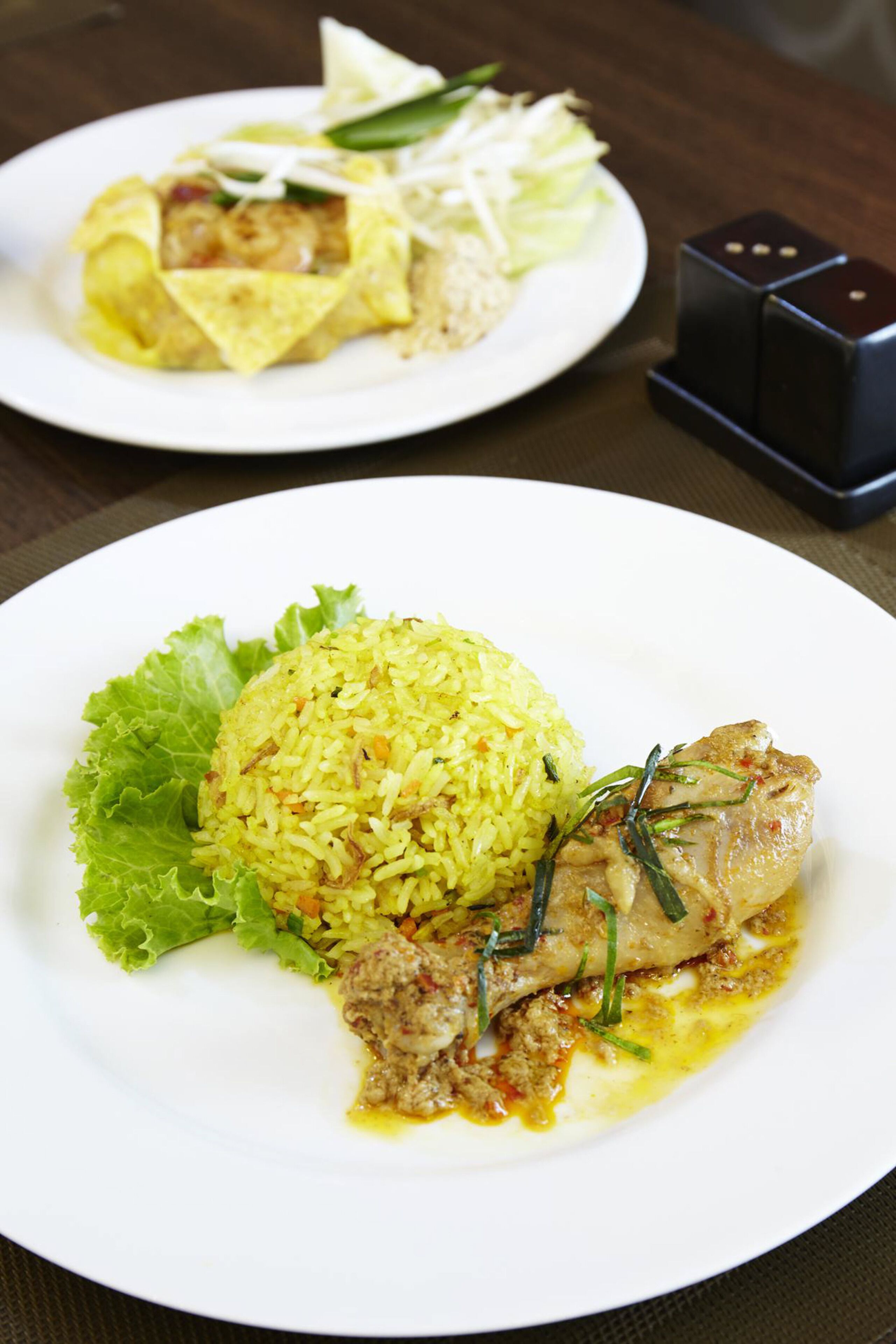A plate of yellow rice with a piece of meat and a lettuce leaf, and another plate with a wrap and vegetables.