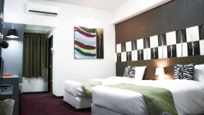 A hotel room with two beds, a desk, a chair, an air conditioning unit, a painting, and a window with curtains. - Baiyoke Boutique (Bangkok)