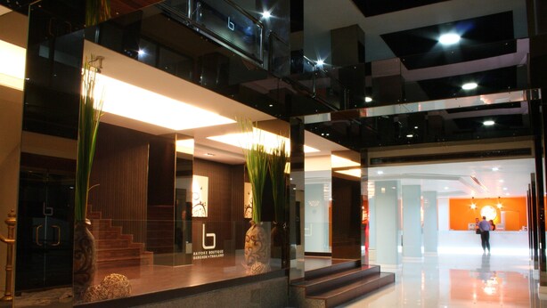 A modern hotel lobby with a reception desk, glass railings, and a staircase leading to upper floors. - Baiyoke Boutique (Bangkok)