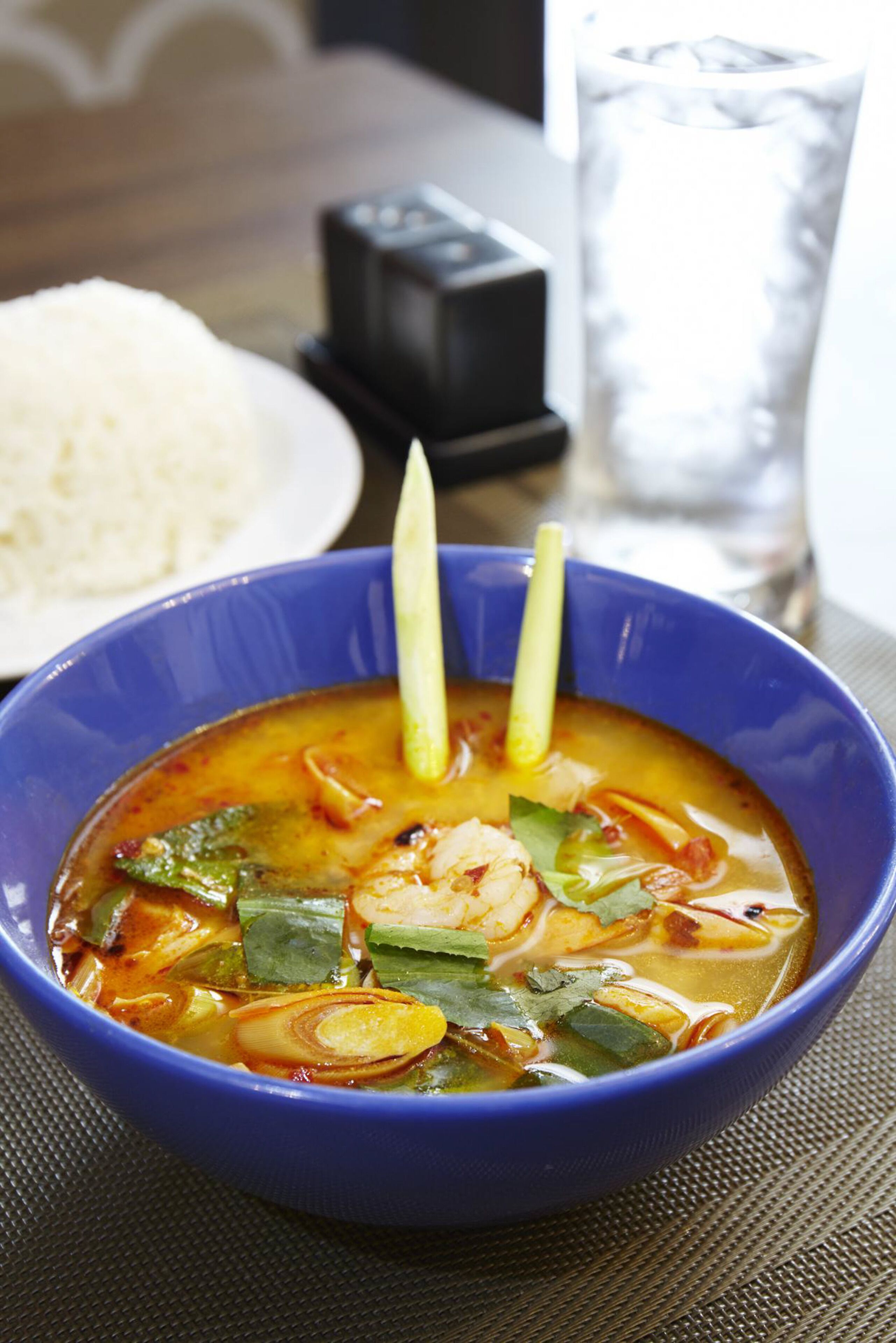 A bowl of soup with a spoon, a glass of water, and a plate of rice on a table.