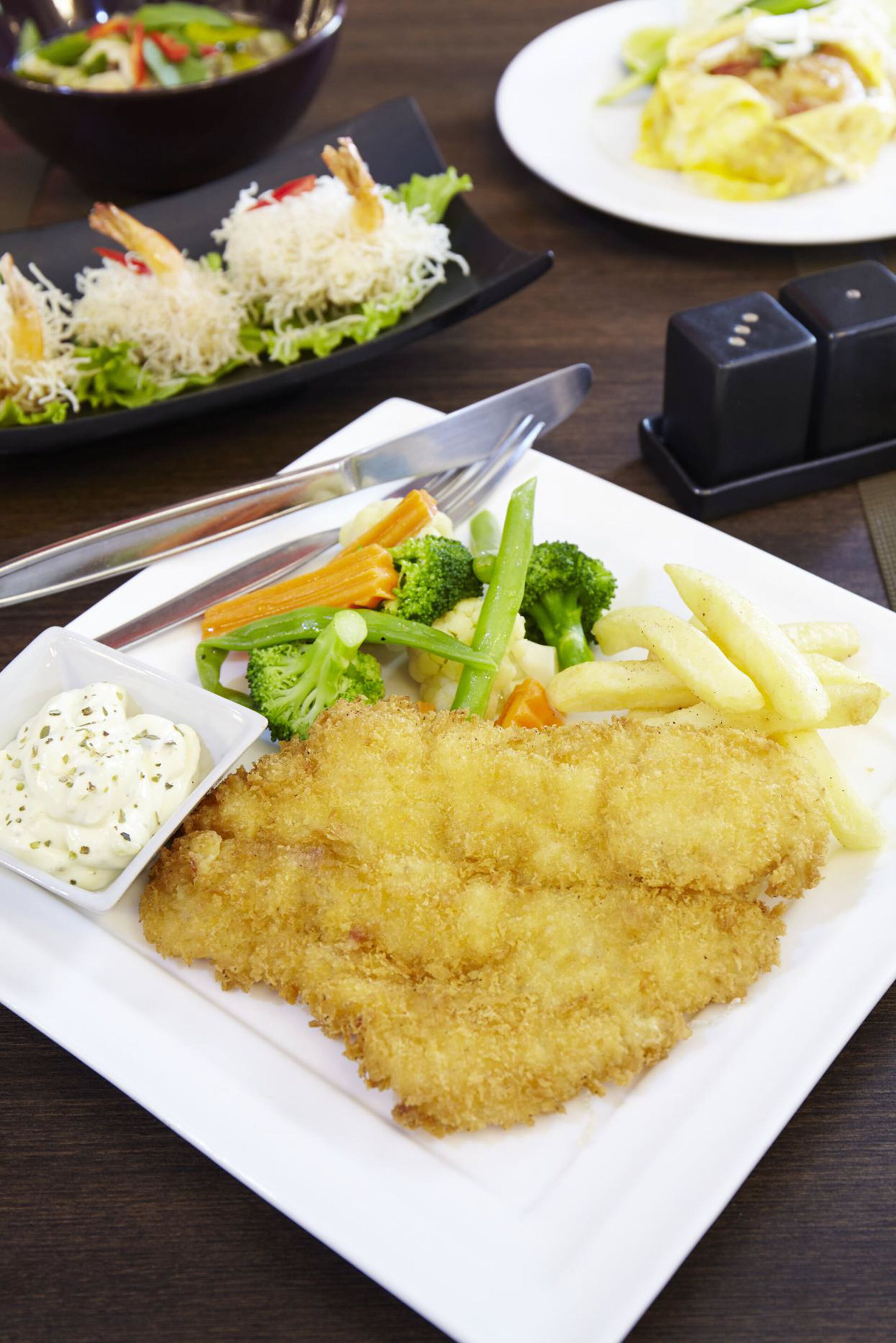A plate of food with a breaded cutlet, vegetables, and a side of sauce.