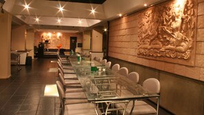 A conference room with a long glass table and white chairs, a stone wall with carvings, and a ceiling with recessed lighting. - Baiyoke Boutique (Bangkok)