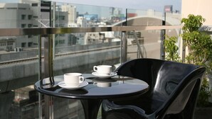 A balcony with a glass table and chairs, a city view, and a plant. - Baiyoke Boutique (Bangkok)
