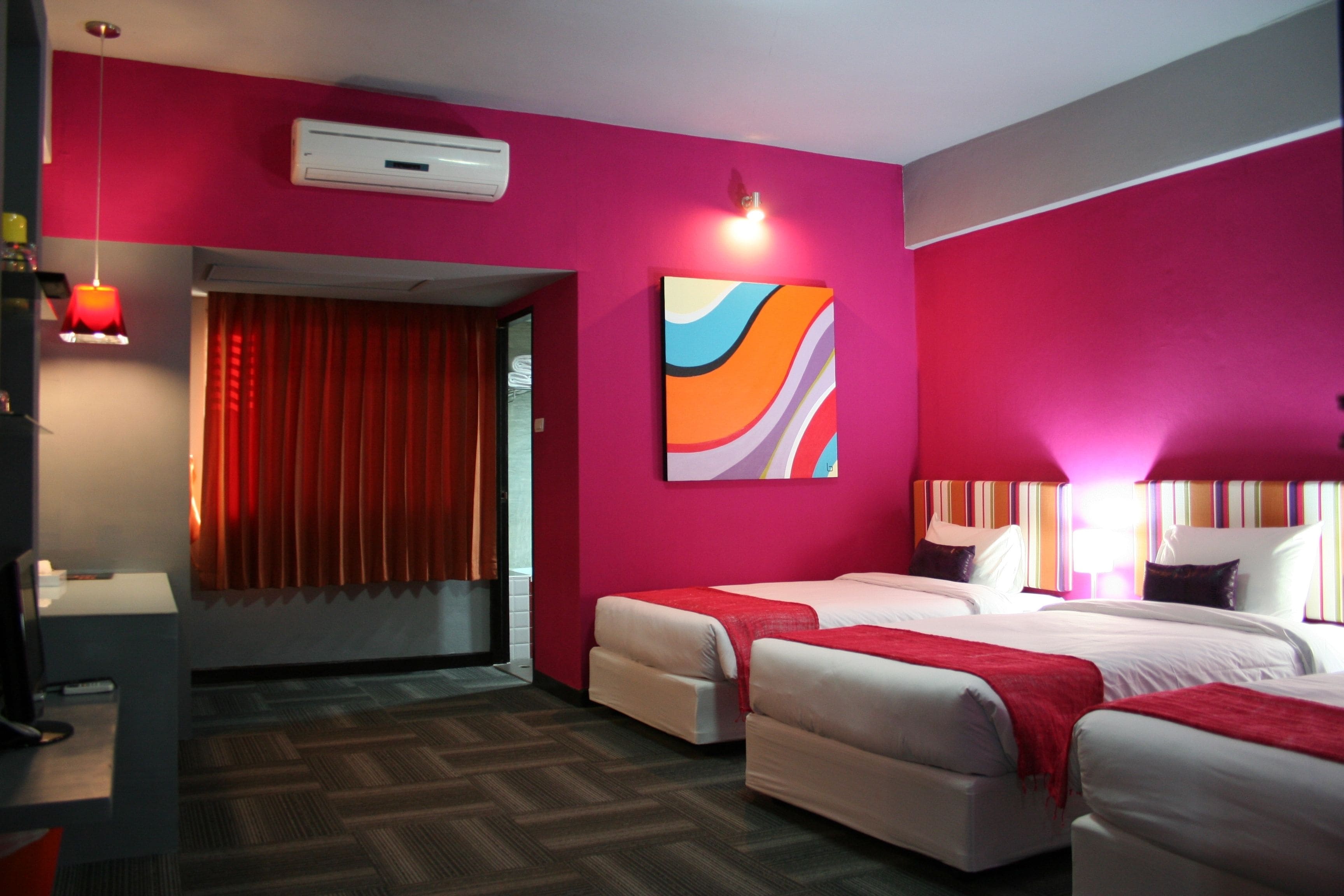 Une chambre d’hôtel avec deux lits, un rideau rouge, un tableau abstrait aux couleurs vives et un appareil de climatisation moderne.