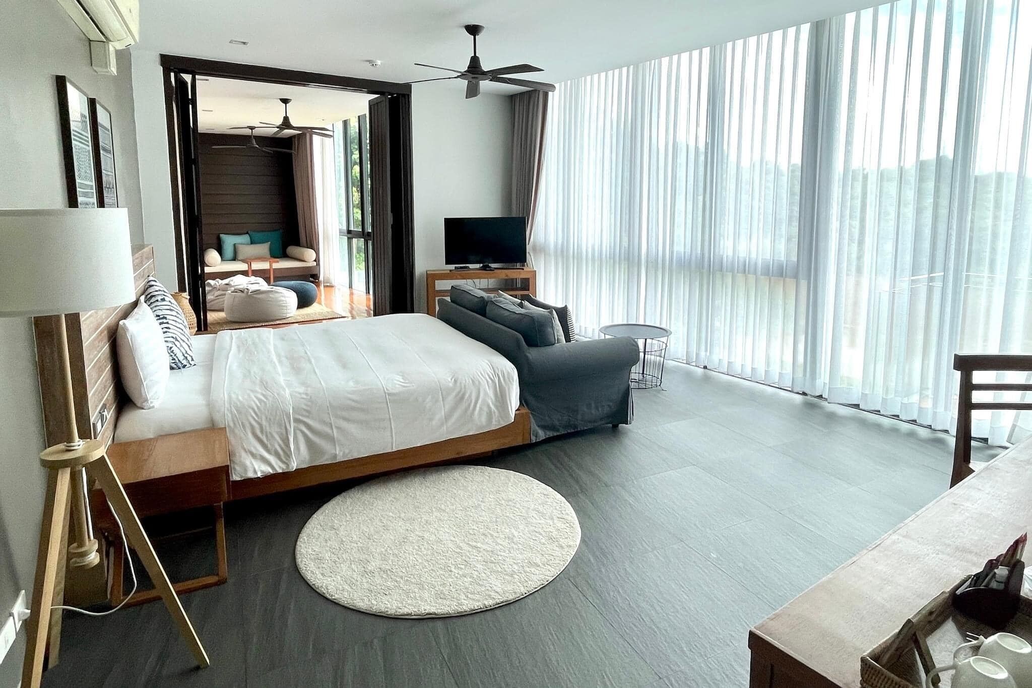 Habitación de hotel moderna con una cama grande, televisión, escritorio y balcón con cortinas.