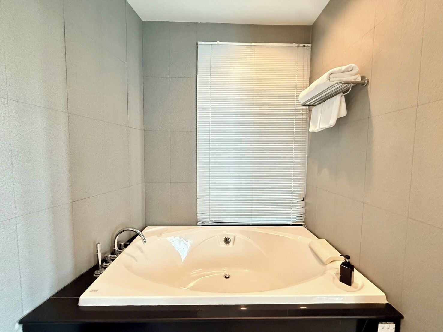 A modern bathroom with a large bathtub, a towel rack with towels, and a window with blinds.