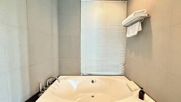 A modern bathroom with a large bathtub, a towel rack with towels, and a window with blinds.