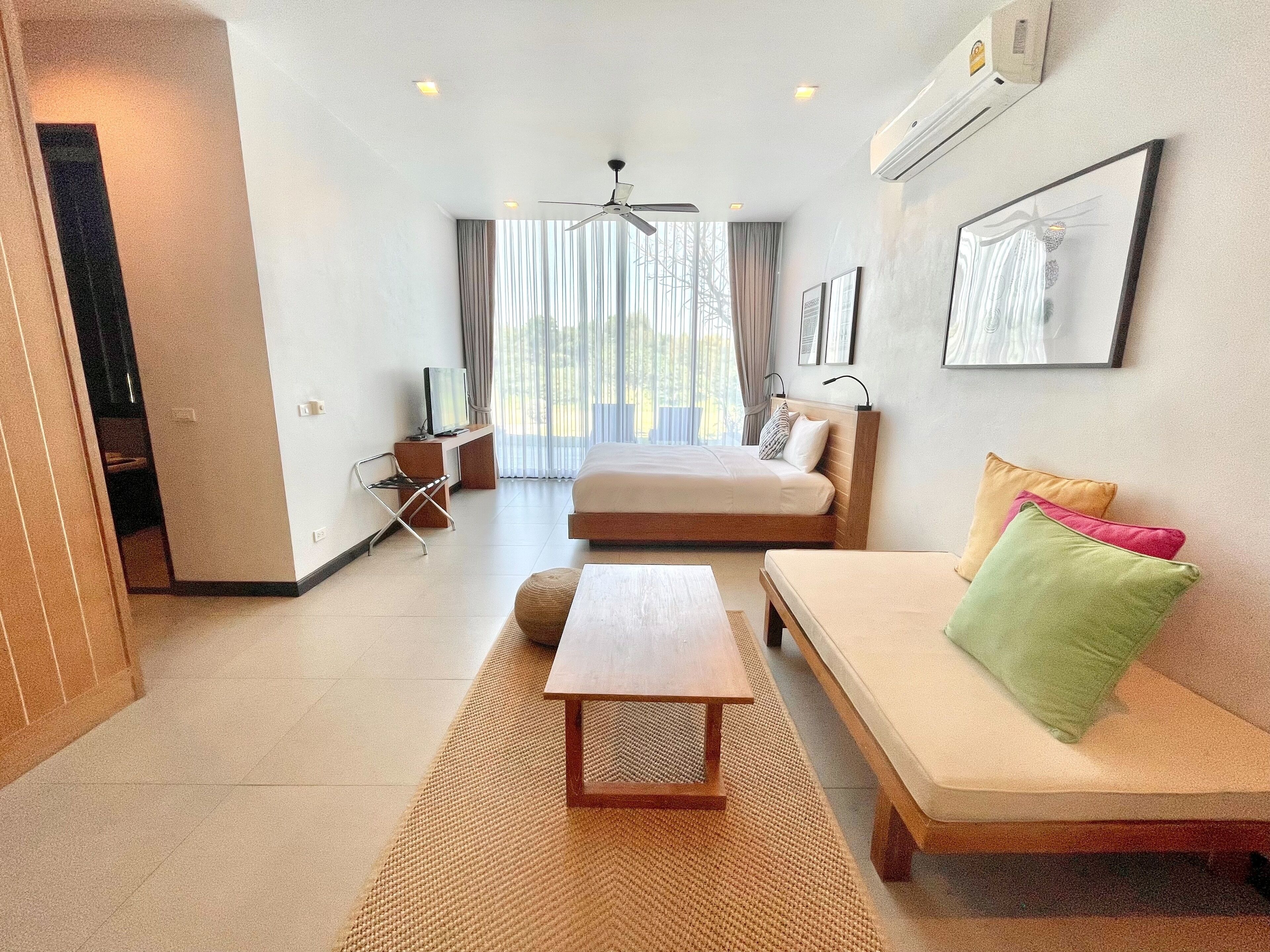 A modern hotel room with a bed, sofa, and a desk with a television.