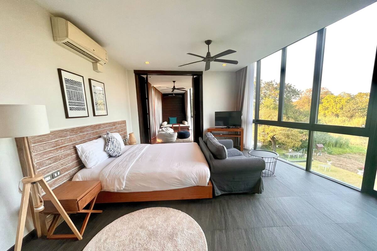 Quarto de hotel moderno com uma cama grande, um sofá, uma TV e vista para o exterior.