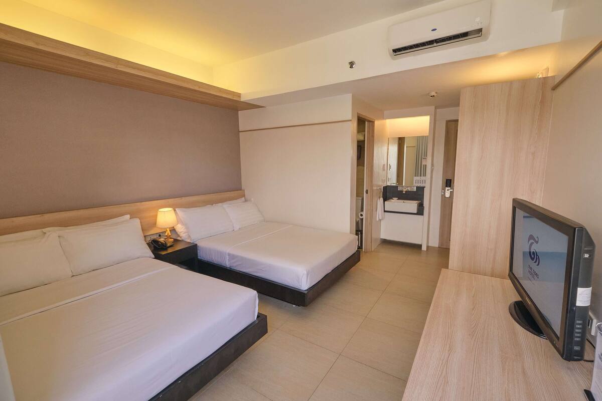 A hotel room with two beds, a desk with a computer, and a bathroom visible through an open door.