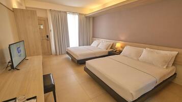 A hotel room with two beds, a desk, a television, and a window with curtains.