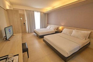 Habitación de hotel con dos camas, un escritorio, un televisor y una ventana con cortinas.