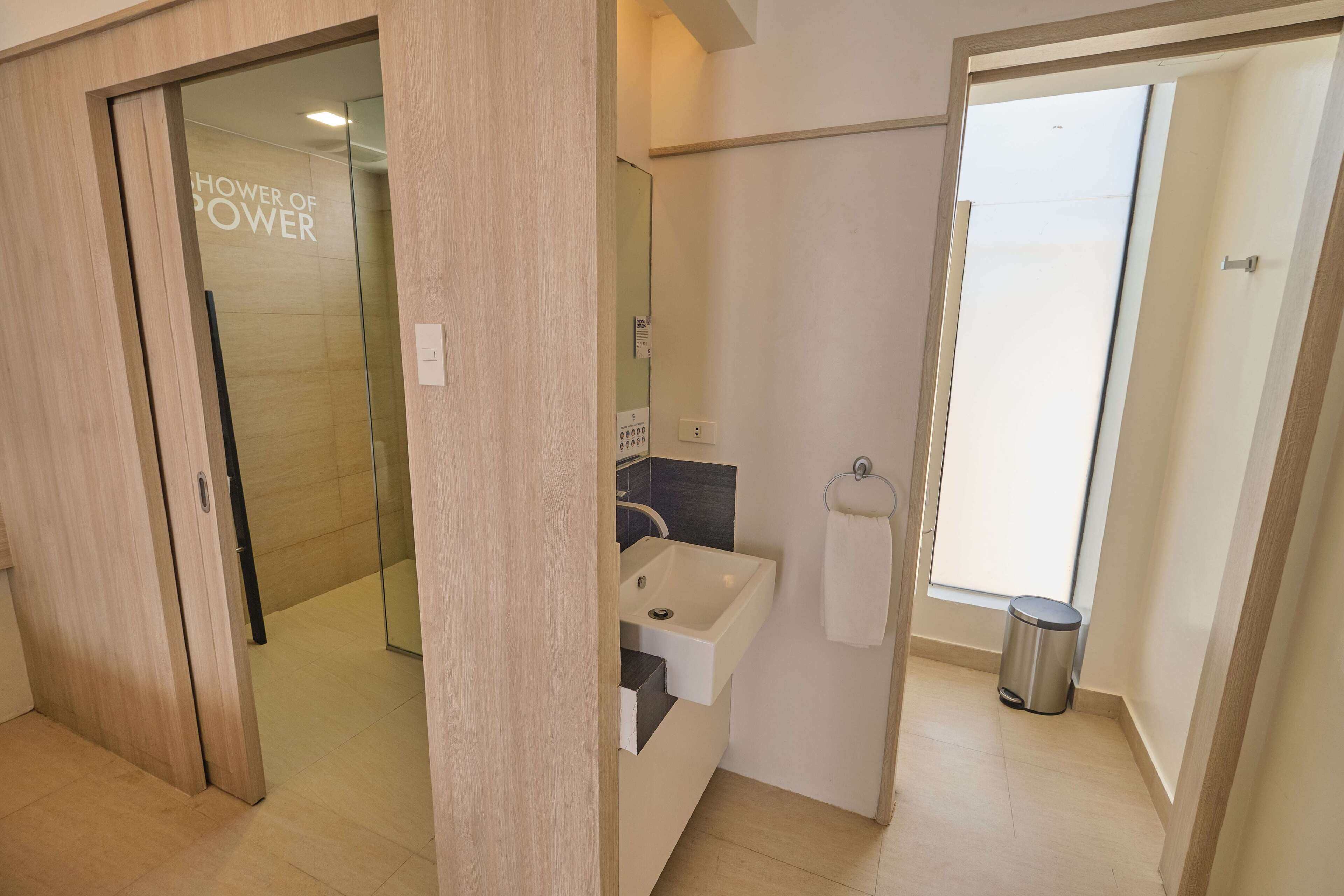 A modern bathroom with a glass shower enclosure, a white sink, and a visible trash bin.