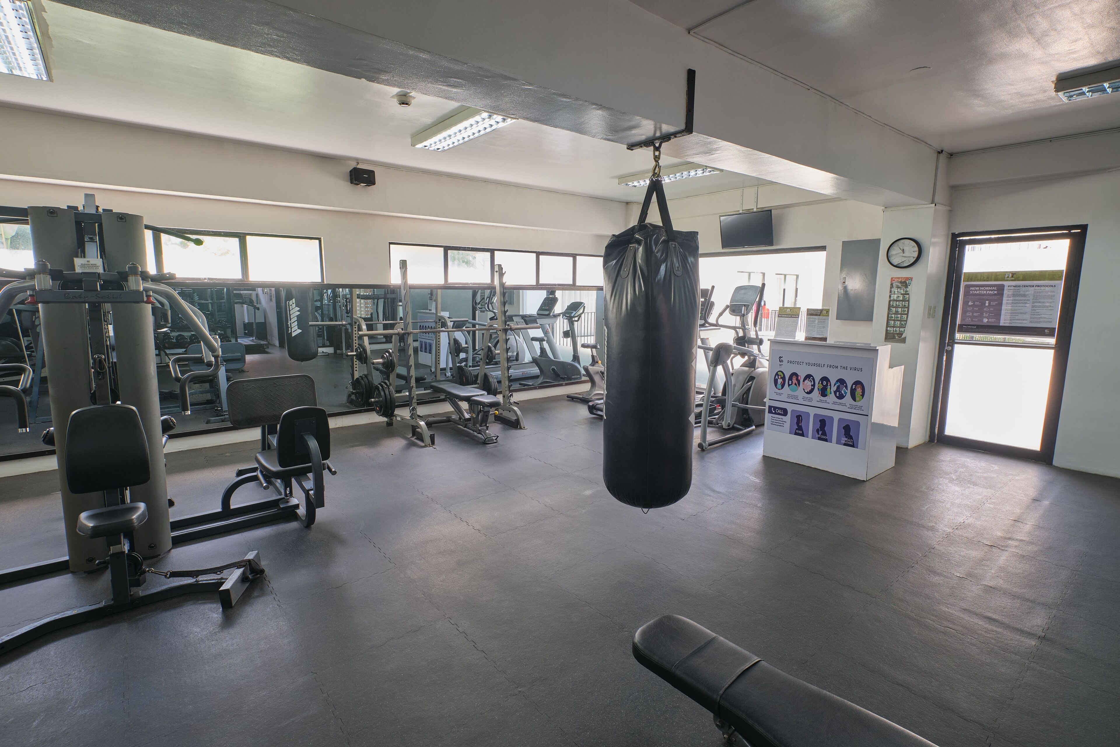 Un gimnasio con varios equipos de ejercicio, un saco de boxeo y una pantalla informativa digital.