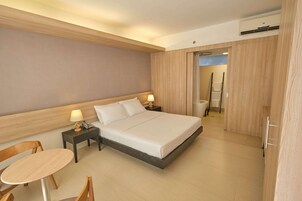 Una habitación de hotel con cama, mesitas de noche, una silla y una pequeña mesa.