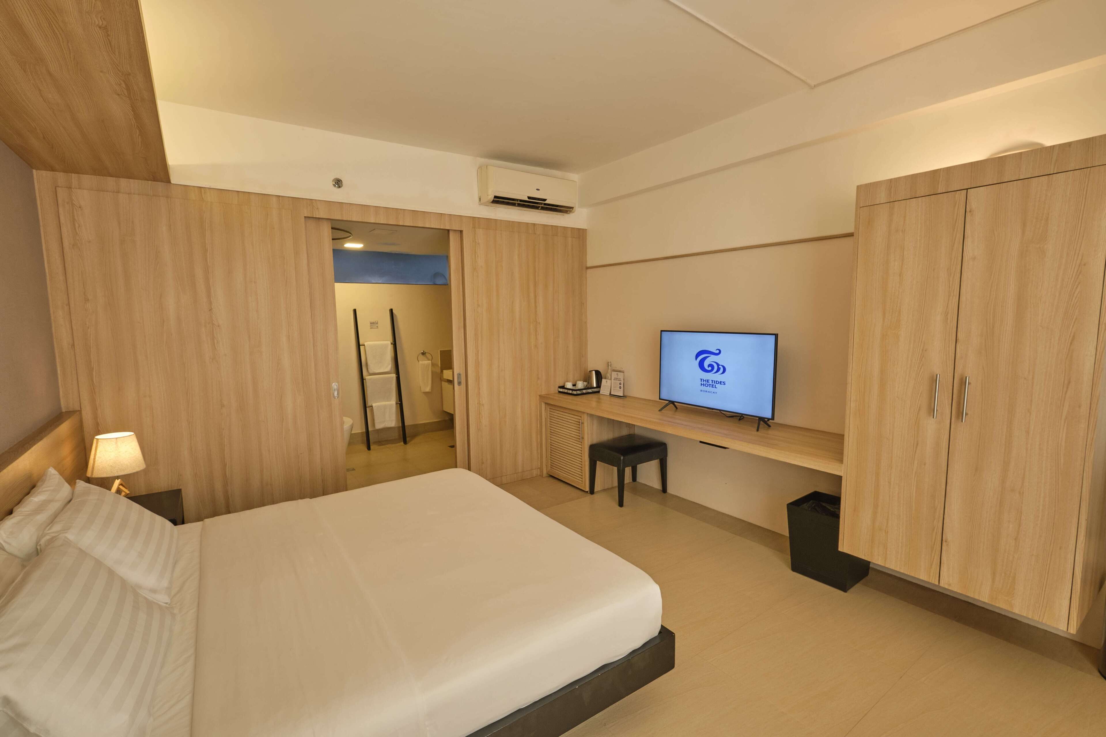 A hotel room with a bed, a desk with a computer, a TV, and wooden wardrobes.