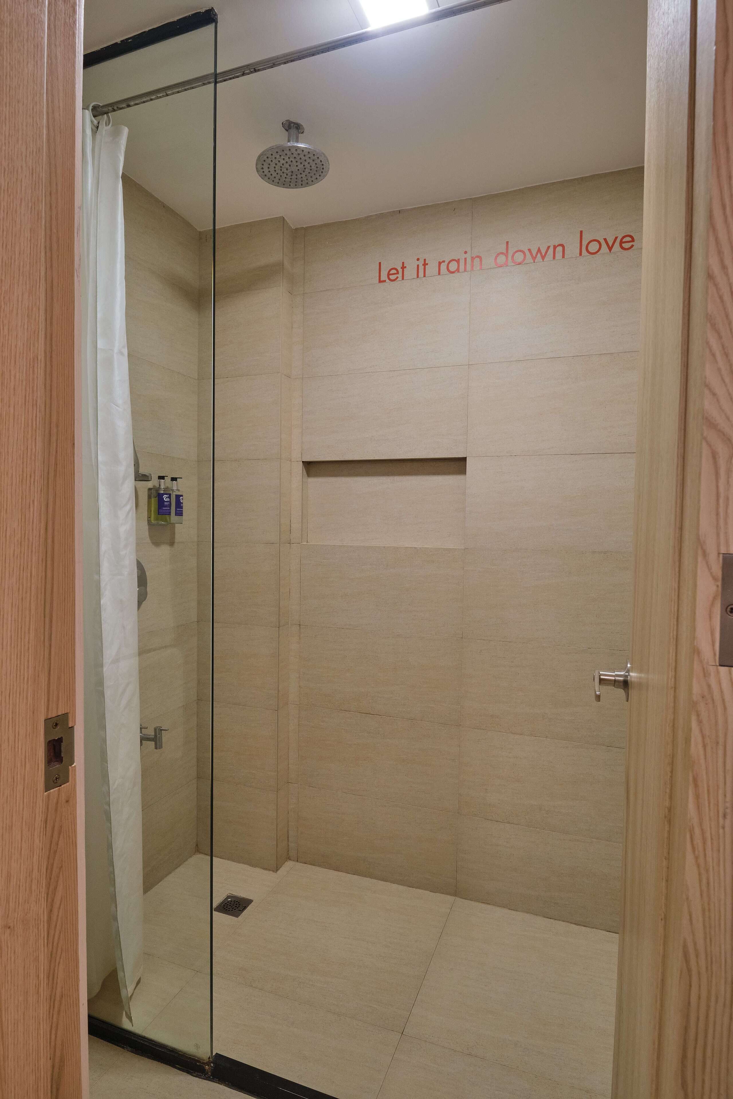 Un espace douche moderne doté d’une porte en verre, d’un pommeau de douche et d’une petite étagère pour les articles de toilette.