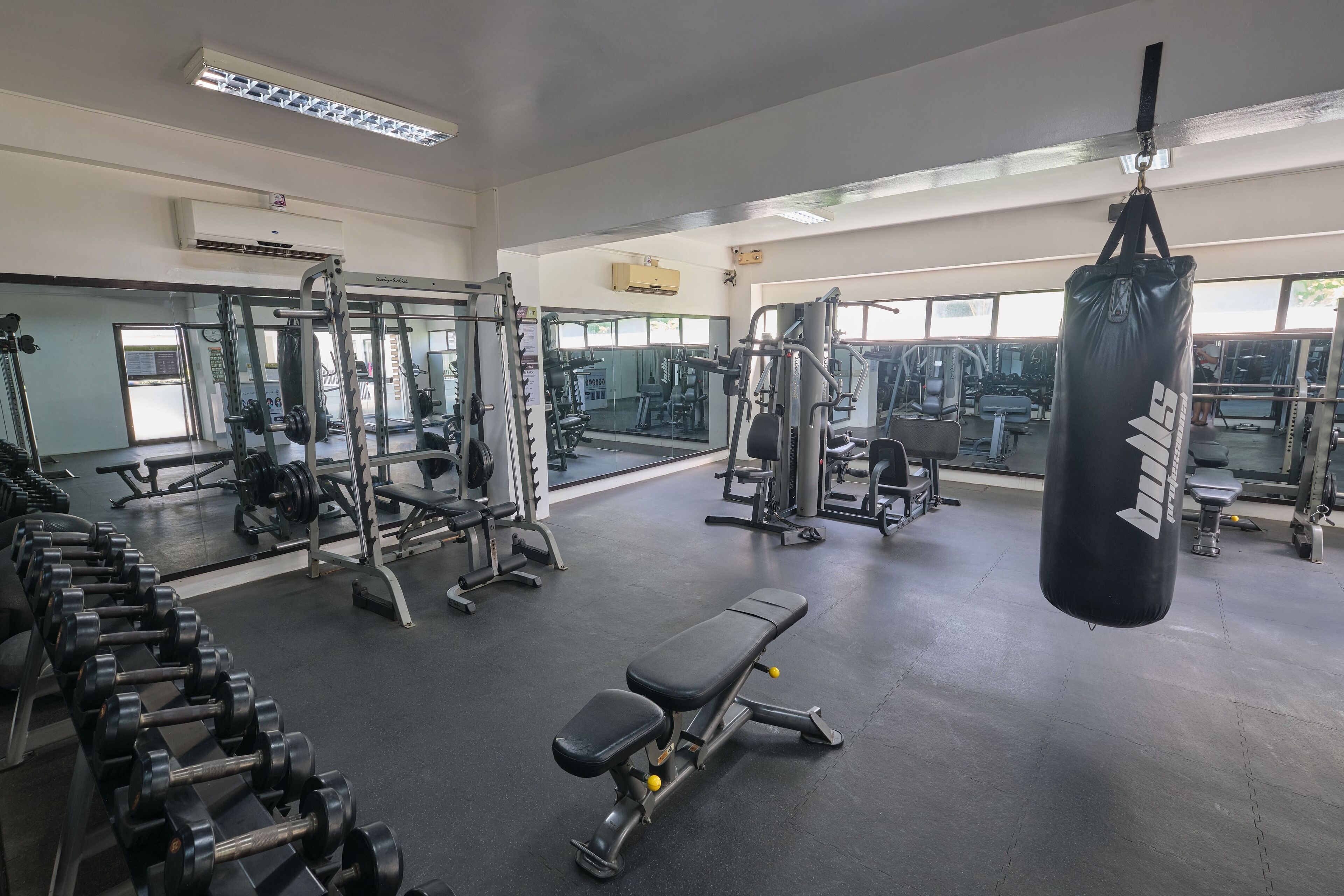 Ein Fitnessraum mit verschiedenen Trainingsgeräten, darunter Hanteln, eine Bank und ein Boxsack.