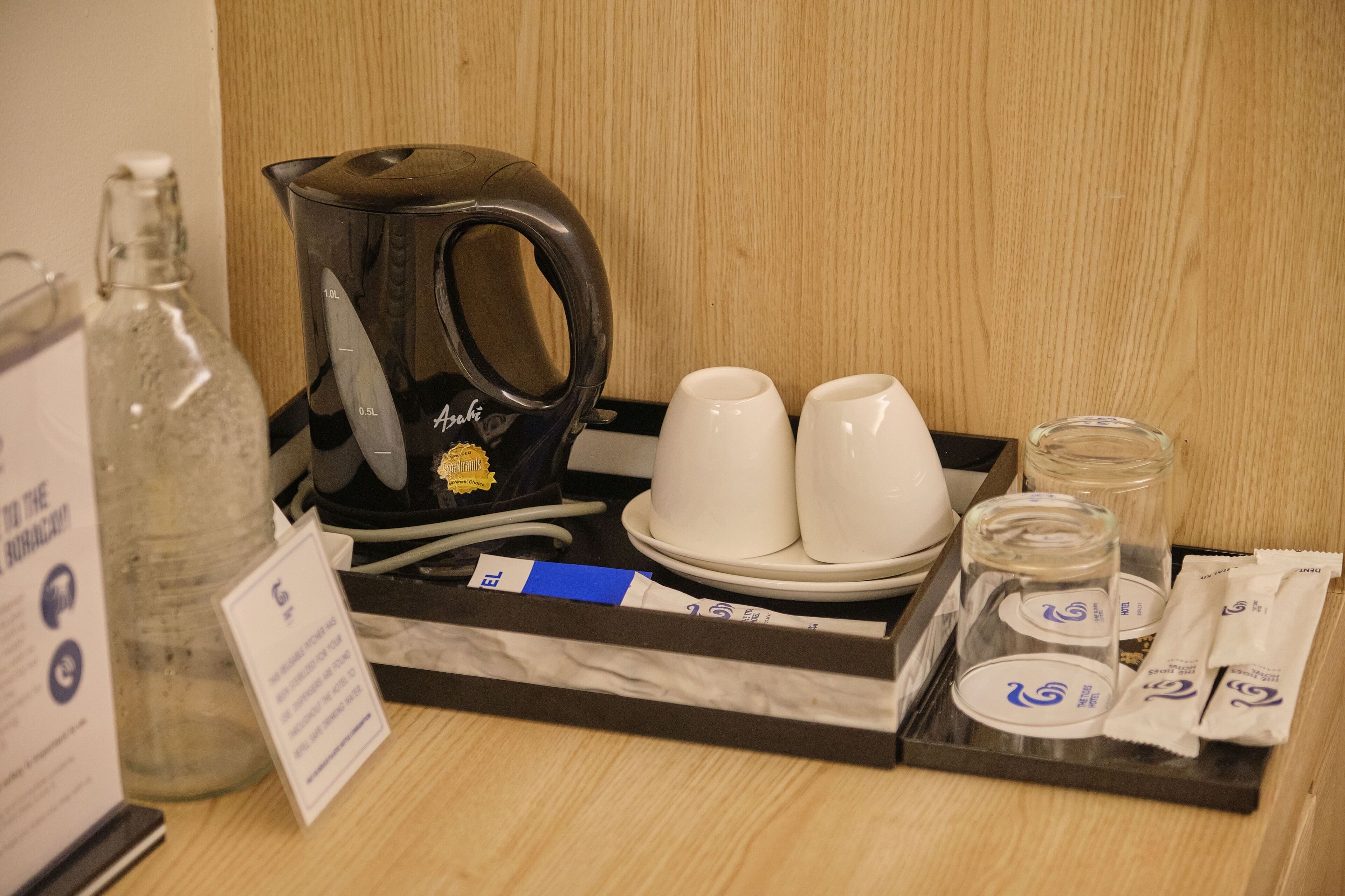A hotel room's breakfast tray with a coffee maker, cups, a glass jar, and packets.