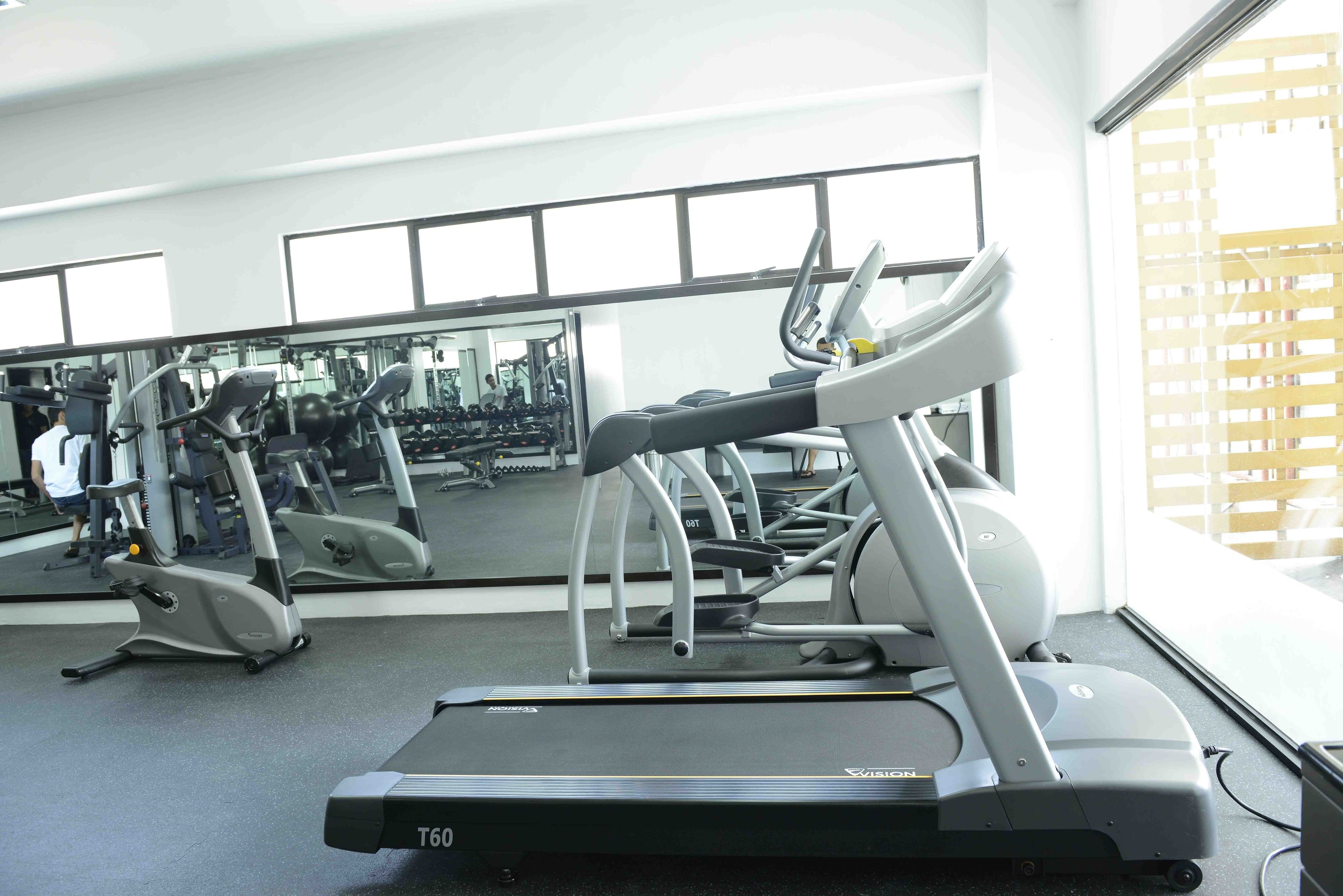 A gym with treadmills, exercise equipment, and a large mirror reflecting the space.
