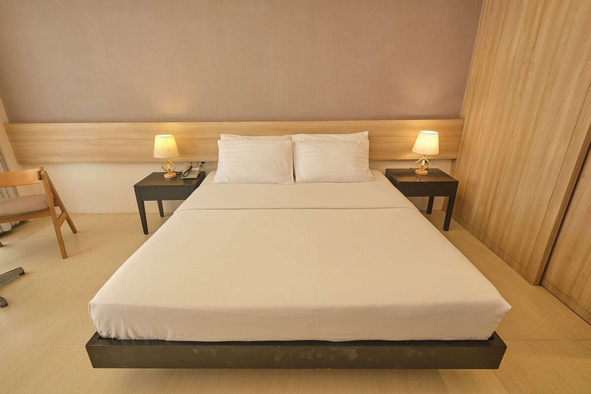 A large bed with white linens, two bedside tables with lamps, a wooden chair, and a wooden headboard.