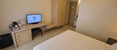 A hotel room with a bed, a desk with a computer, a wardrobe, and a trash bin.